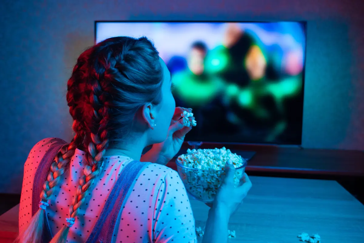 Nuori nainen katsoo tv:tä ja syö popcornia.