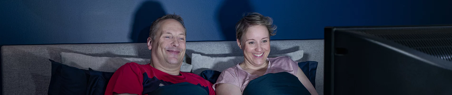 Mies ja nainen katsovat televisiota sängystä.