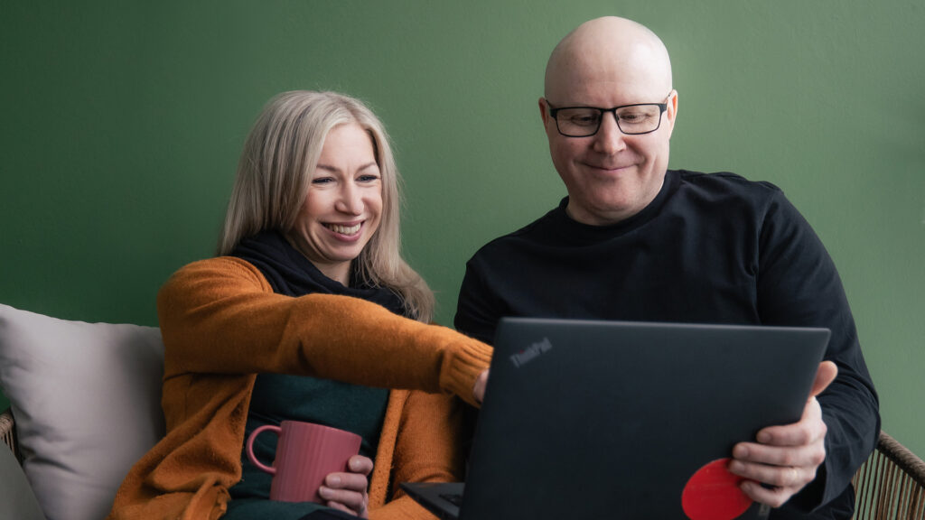 Mies ja nainen katselevat tietokoneen näyttöä. Nainen osoittaa näyttöä. Naisella on kahvimuki kädessään. 